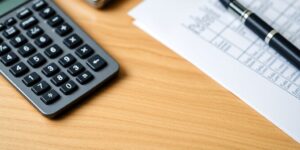 Nahaufnahme eines Rechners und Finanzdokumenten auf Tisch.